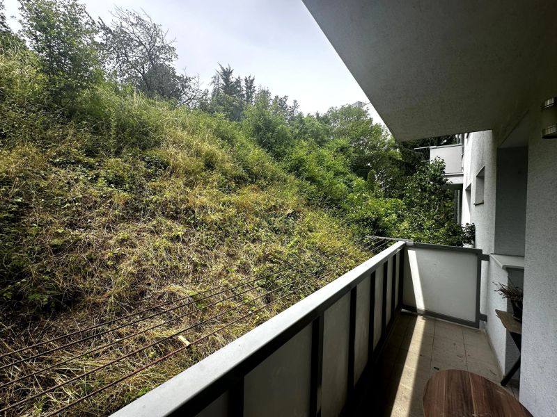 Balkon einer 2-Zimmer-Wohnung mit Blick auf einen Hang mit dichtem Bewuchs.