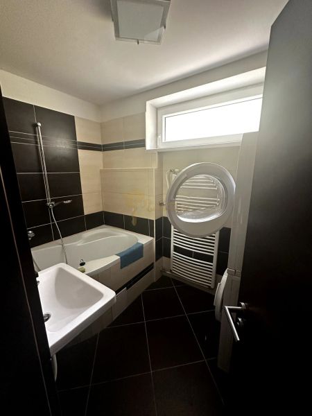 Badezimmer in einer 2-Zimmer-Wohnung mit Badewanne, Waschbecken und Waschmaschine; schwarze und beige Fliesen.