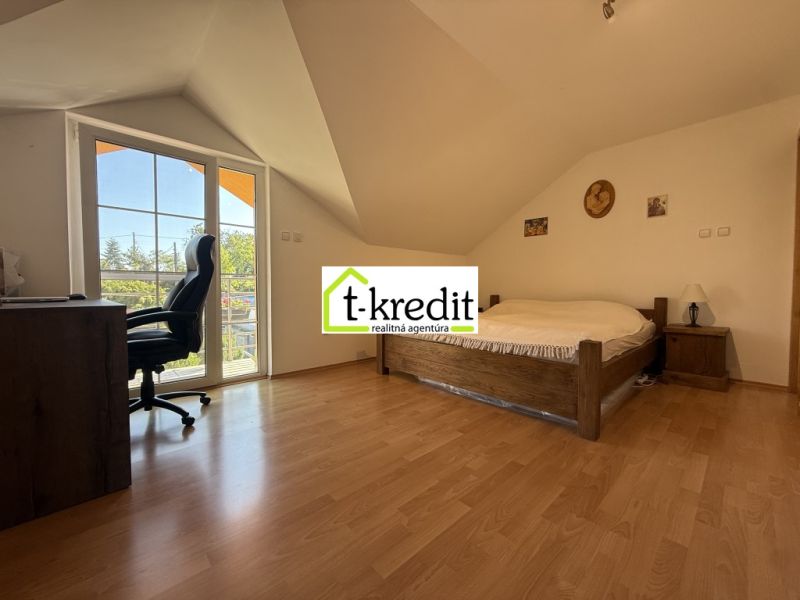 Ein Schlafzimmer im Dachgeschoss eines Einfamilienhauses mit einem Bett, einem Boden in Holzoptik und einem Schreibtisch.