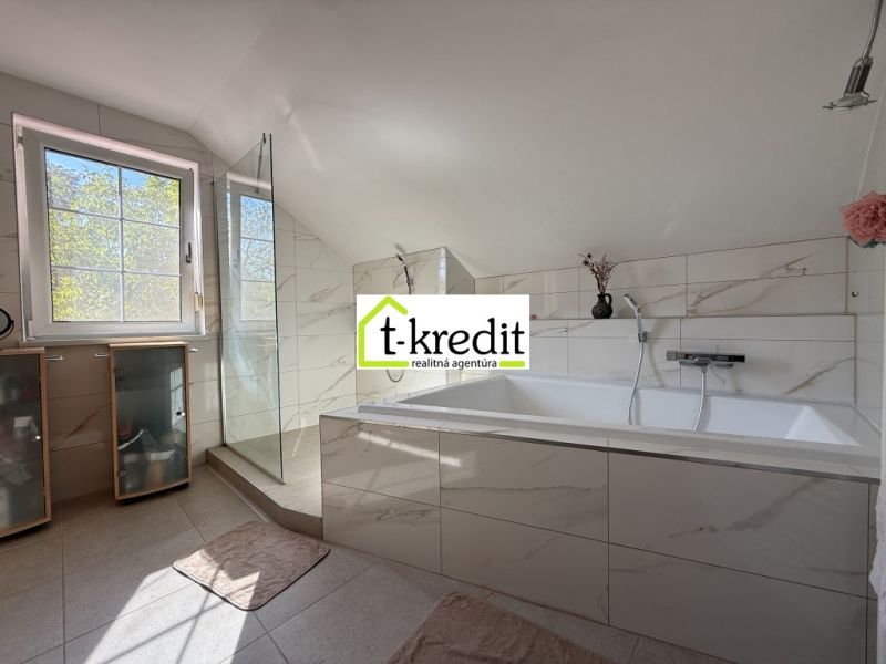 Ein Badezimmer in einem Einfamilienhaus mit einer Badewanne und einer Dusche, umgeben von Fliesen.