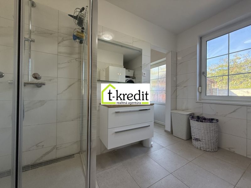 Ein Badezimmer in einem Einfamilienhaus mit weißen Fliesen, einer Dusche und Stauraum.