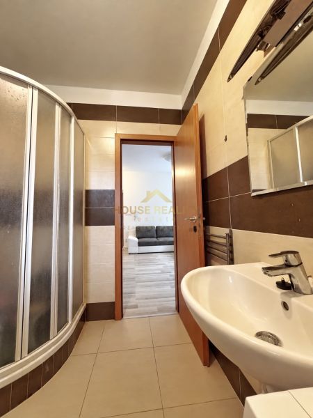Badezimmer in einem Studio-Apartment mit Waschbecken, Duschkabine und braun-beigen Fliesen.