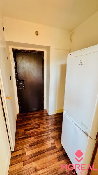 Ein Interieur mit einem Kühlschrank und einem Holzboden in einem Einzimmerapartment.