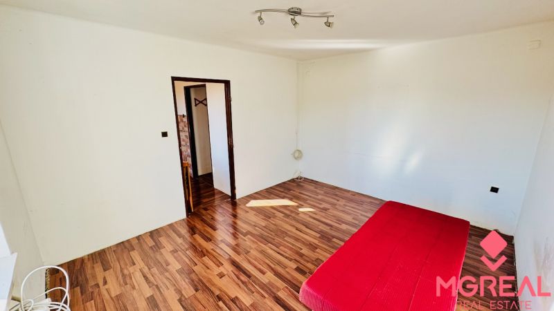 Ein Zimmer in einer Einzimmerwohnung mit einer roten Matratze und einem Boden in Holzoptik.