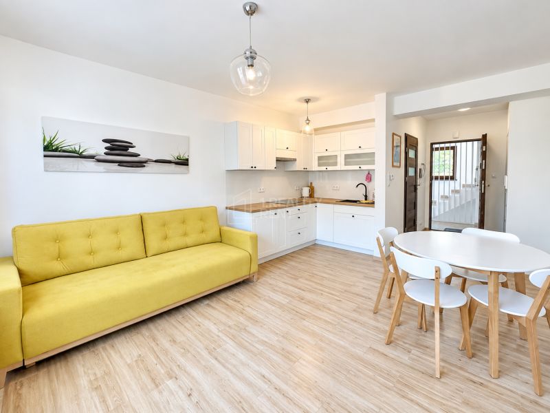Wohnzimmer in einer Einzimmerwohnung mit Holzboden und gelbem Sofa.