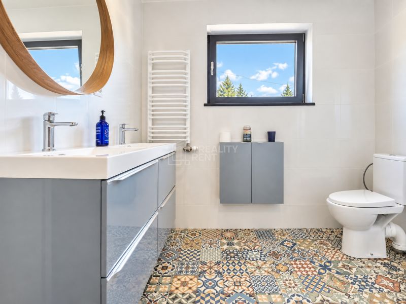 Badezimmer mit Mosaikboden, modernem Waschbecken und Fenster in einer Einzimmerwohnung.