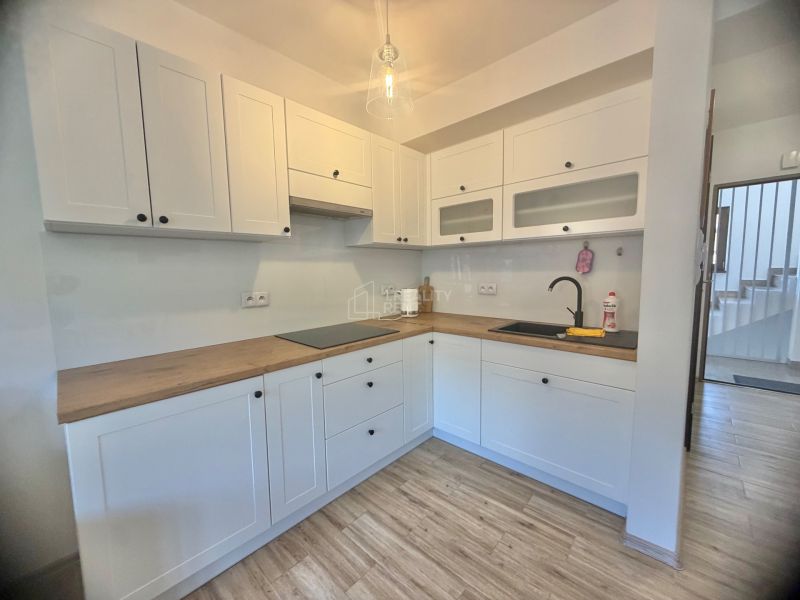 Küche in einer Einzimmerwohnung mit weißen Schränken und einem Boden in Holzoptik.