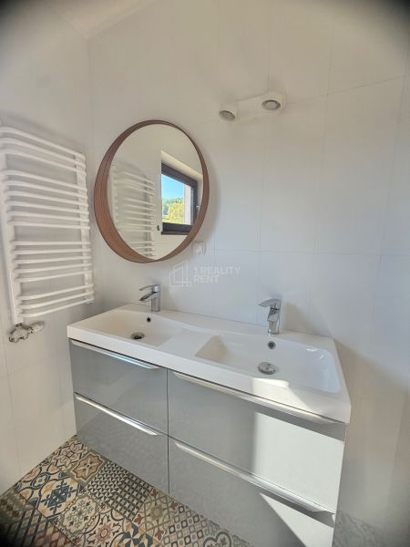 Das Badezimmer in der Einzimmerwohnung enthält ein Doppelwaschbecken, einen runden Spiegel und gemusterte Fliesen.