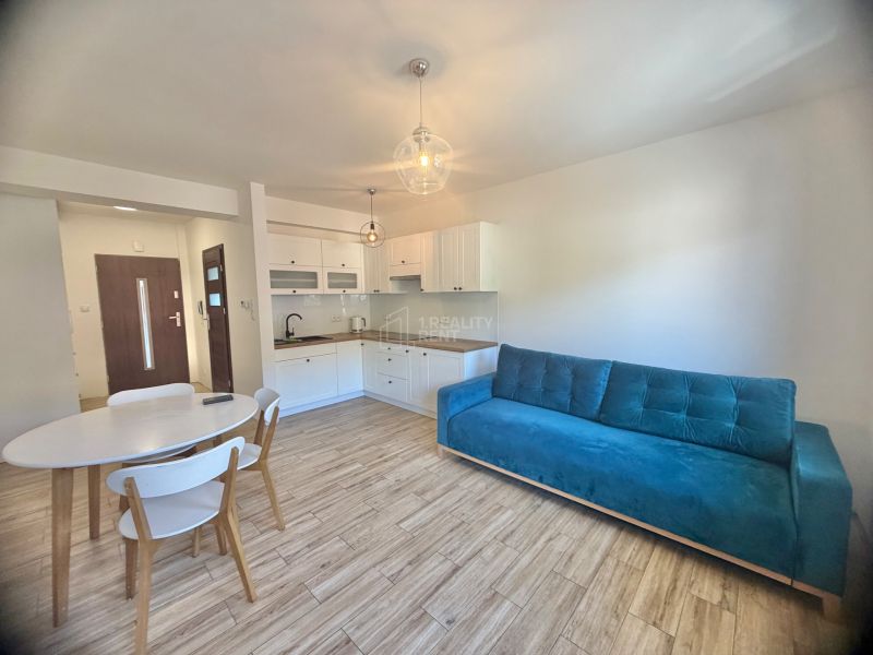 Küche in einer Einzimmerwohnung mit Holzboden, weißen Möbeln und einem blauen Sofa.
