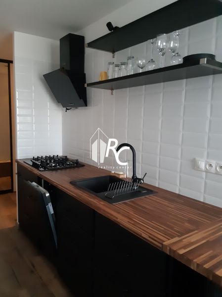 Küche in einer 2-Zimmer-Wohnung mit schwarzer Dunstabzugshaube, weißen Fliesen und einem Boden in Holzoptik.