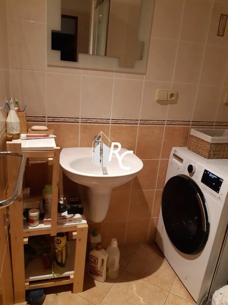 Badezimmer mit Spiegel und Waschmaschine in einer 2-Zimmer-Wohnung mit beigen Fliesen.