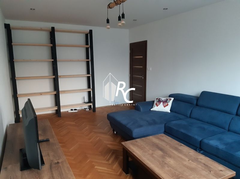 Wohnzimmer mit blauem Sofa, Fernseher und Regalen in einer Zweizimmerwohnung, Holzboden mit Holzdekor.