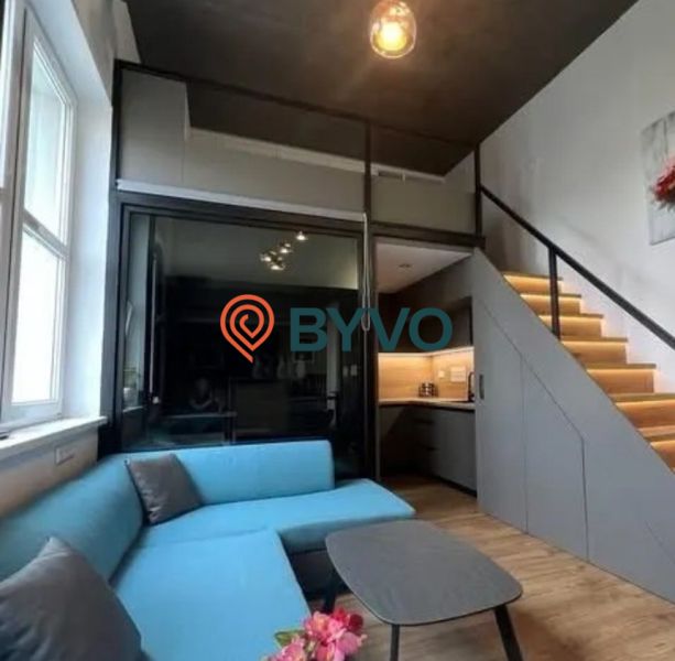 Wohnzimmer mit blauem Sofa und Treppe in einem Einzimmerapartment.