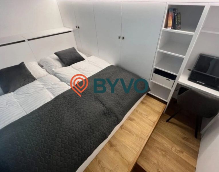 Schlafzimmer in einer Einzimmerwohnung mit Doppelbett und Stauraum, Boden mit Holzdekor.