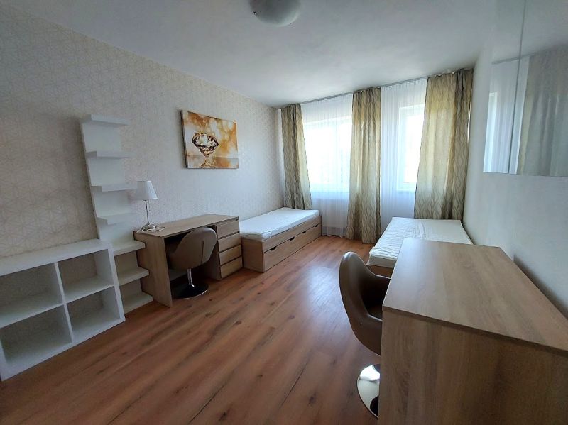 Ein Zimmer mit zwei Betten, Tischen und einem Boden mit Holzdekor in einer 3-Zimmer-Wohnung.