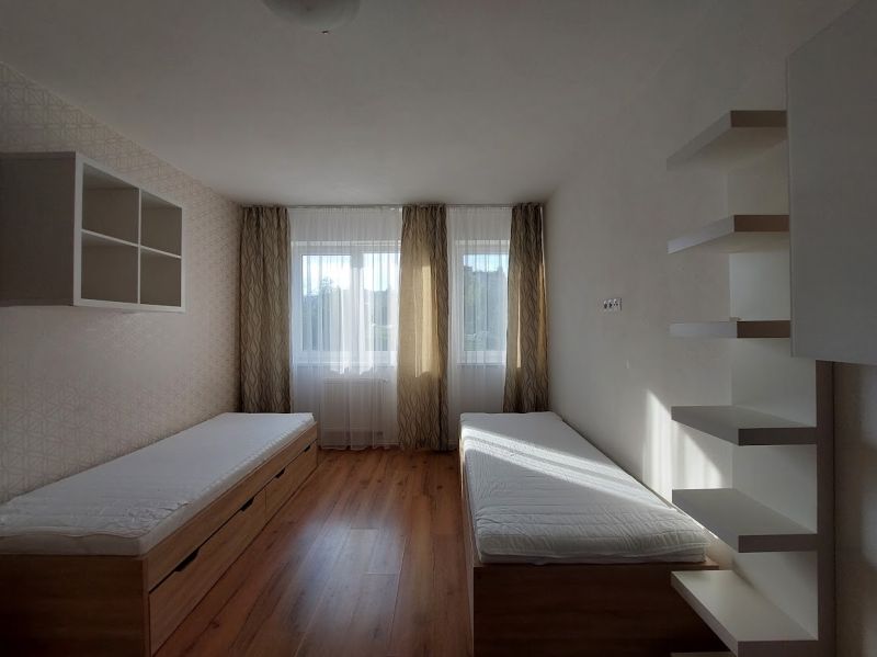 Ein Zimmer mit zwei Betten, Regalen und einem Boden in Holzoptik in einer 3-Zimmer-Wohnung.