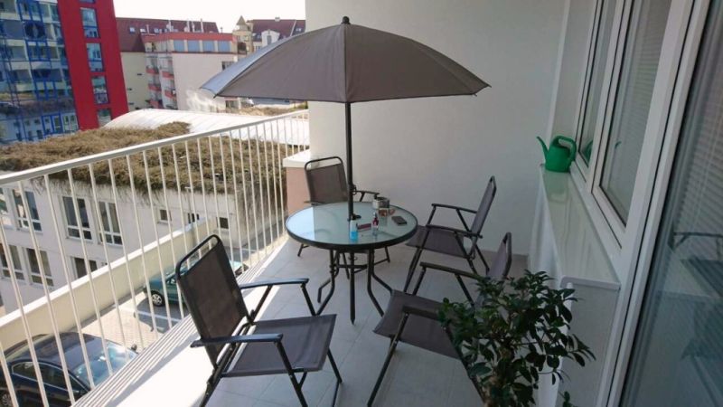 Balkon einer 3-Zimmer-Wohnung Nad Plážou in Banská Bystrica mit Sitzgelegenheit und Sonnenschirm.