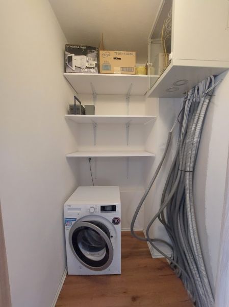 Technikraum in einer 3-Zimmer-Wohnung mit Waschmaschine und Regalen, Boden mit Holzdekor.