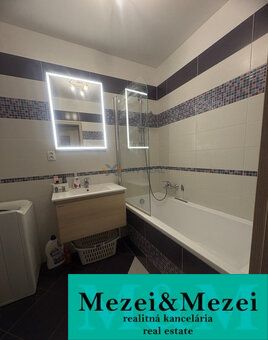 Badezimmer mit Spiegel und Badewanne in einer 2-Zimmer-Wohnung; weiße Fliesen kombiniert mit Mosaik.
