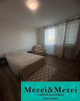 Schlafzimmer in einer 2-Zimmer-Wohnung mit Bett, Sessel und Boden in Holzoptik.