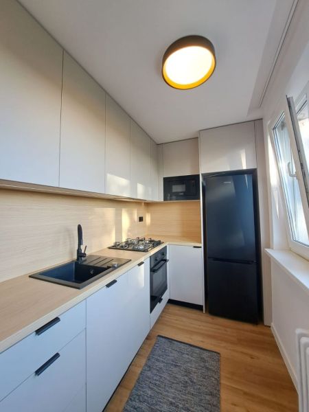 Küche in einer 2-Zimmer-Wohnung mit weißen Schränken und einem Boden in Holzoptik.