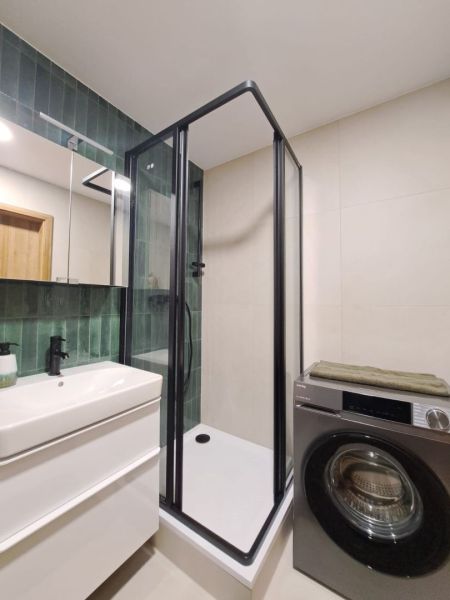 Badezimmer einer 2-Zimmer-Wohnung mit moderner Duschkabine, Waschmaschine und grünen Fliesen.