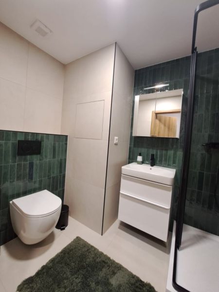 Badezimmer in einer 2-Zimmer-Wohnung mit dunkelgrünen Fliesen und weißen Sanitäreinrichtungen.