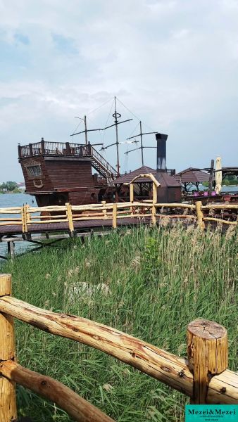 Ein Holzboot als Attraktion bei der Hütte an den Seen von Senec, hinter einem Holzzaun.