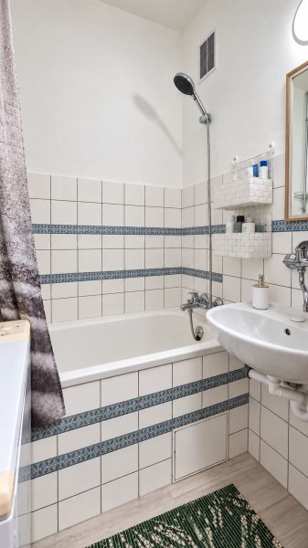 Badezimmer mit Badewanne, Waschbecken, weißen Fliesen und gemusterten Details in einer 3-Zimmer-Wohnung.