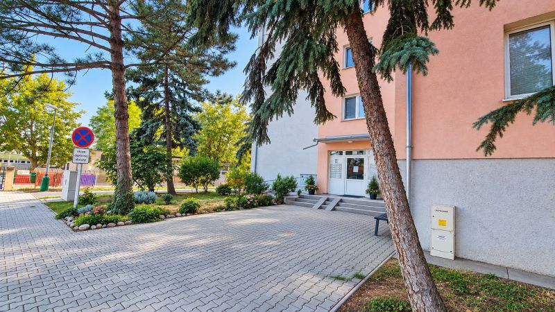 Eingang in eine 3-Zimmer-Wohnung in Pezinok in der Straße Za hradbami, umgeben von Grünflächen und Pflastersteinen.
