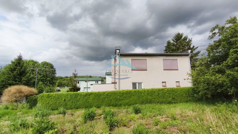 Ein Einfamilienhaus in Nenince, umgeben von dichtem Grün und Bäumen unter einem bewölkten Himmel.