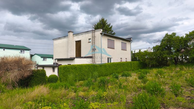 Ein Einfamilienhaus in Nenince, umgeben von Grün und einer Hecke unter einem bewölkten Himmel.