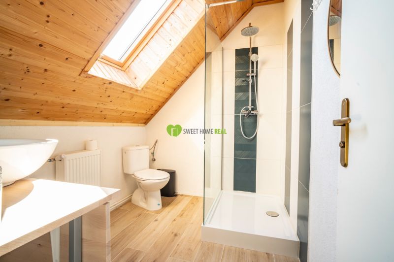 Ein Badezimmer im Dachgeschoss mit Waschbecken, Dusche und einem Boden in Holzoptik.