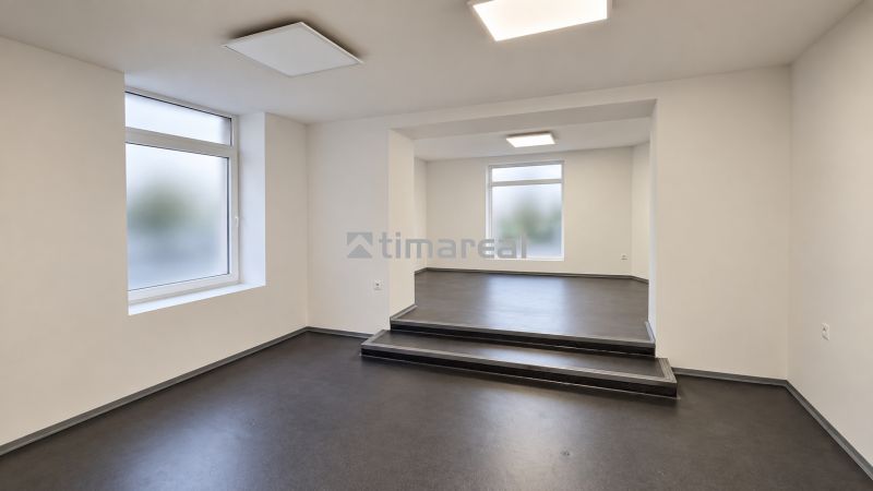 Ein helles Büro mit einem dunklen Boden in Holzoptik und einer Treppe im Raum.