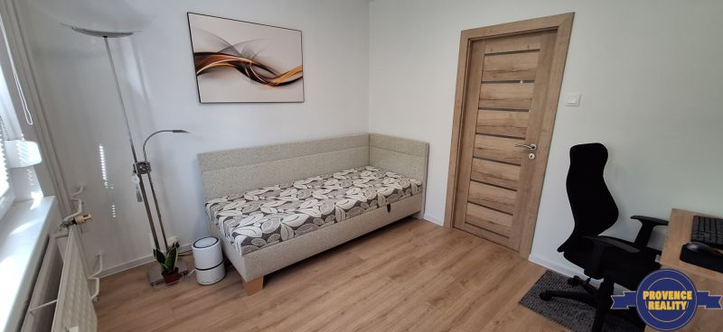 Ein Zimmer in einer 3-Zimmer-Wohnung mit einem Boden in Holzoptik, einem Sofa und einem Bürostuhl.