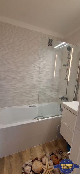 Badezimmer in einer 3-Zimmer-Wohnung mit Badewanne, weißen Fliesen und einem Boden in Holzoptik.