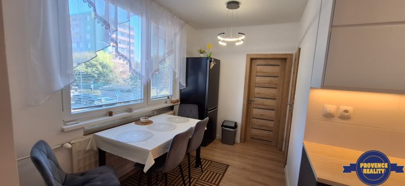 Essbereich mit Fenster, dunkler Kühlschrank, Vorhänge und Tisch in einer 3-Zimmer-Wohnung.