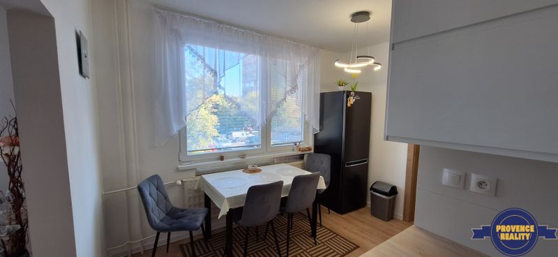 Essbereich in einer 3-Zimmer-Wohnung mit einem dunklen Kühlschrank und einem Boden in Holzoptik.