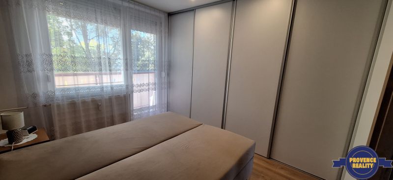 Schlafzimmer in einer 3-Zimmer-Wohnung mit einem großen Kleiderschrank und einem Fenster mit Vorhängen.
