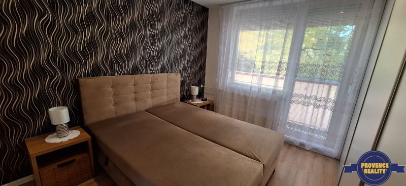 Schlafzimmer mit gepolstertem Bett, gemusterte Tapete, Vorhänge, Boden mit Holzdekor.