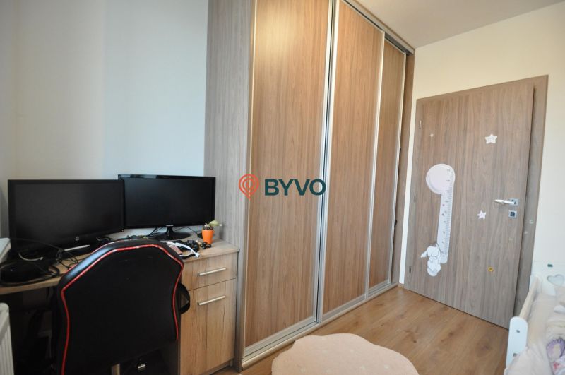 Arbeitsbereich mit Schreibtisch, zwei Monitoren, Kleiderschrank und Boden mit Holzdekor.