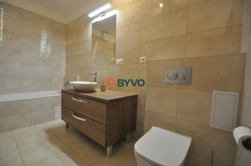 Badezimmer mit Badewanne, Waschbecken auf Holzdekor und beigen Fliesen in einer 3-Zimmer-Wohnung.