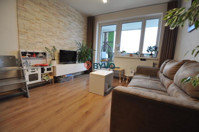 Wohnzimmer in einer 3-Zimmer-Wohnung mit Holzboden und Steinverkleidung an der Wand.