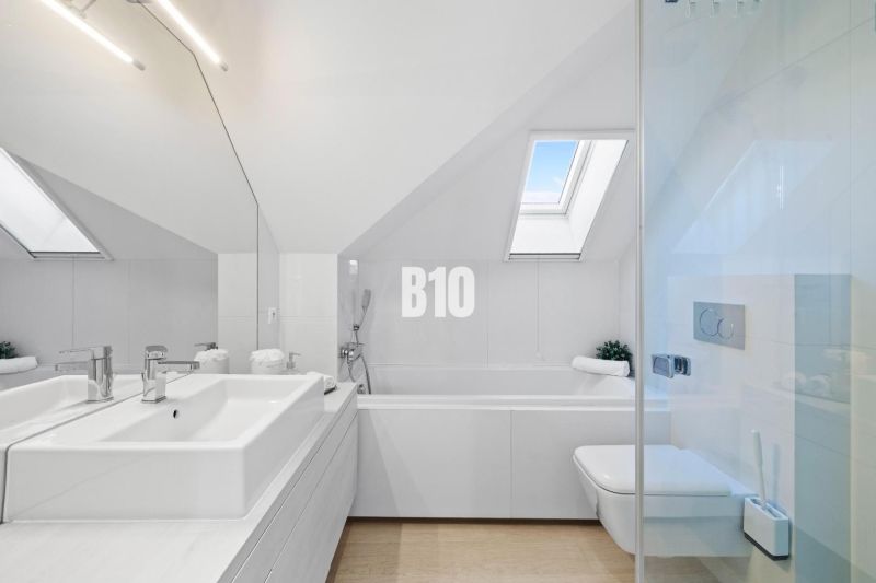 Badezimmer in einer 2-Zimmer-Wohnung mit Badewanne und Dachfenstern, Boden mit Holzdekor.