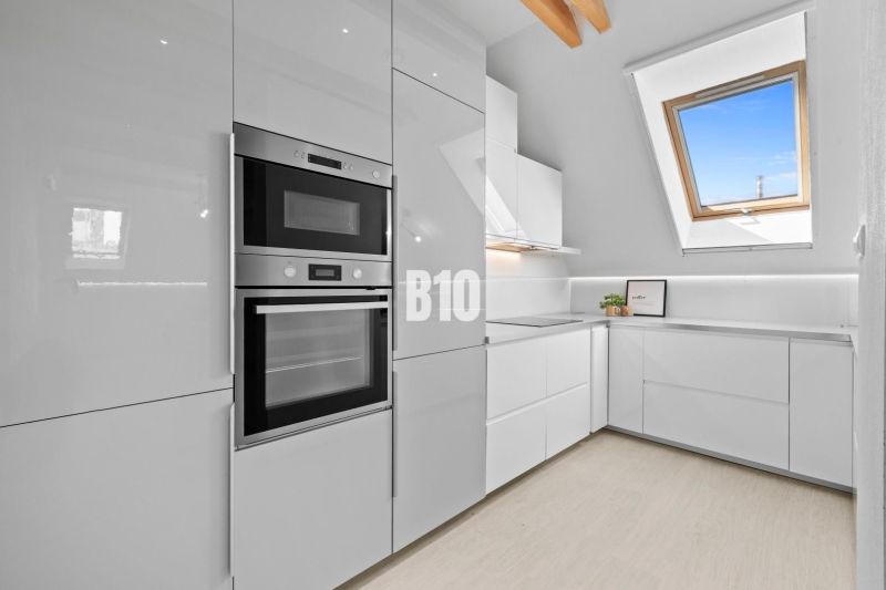 Moderne Küche in einer 2-Zimmer-Wohnung mit weißen Schränken und Dachfenster.