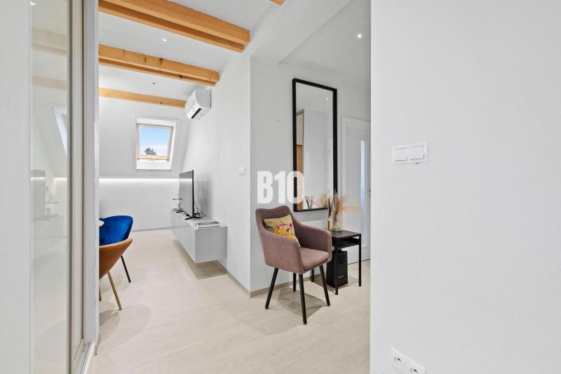 Innenraum einer 2-Zimmer-Wohnung mit Holzboden, Dachfenstern und dekorativen Balken.