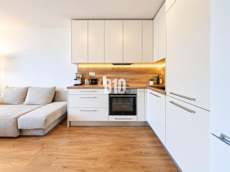 Küche in einer 2-Zimmer-Wohnung mit Holzboden und weißen Schränken.