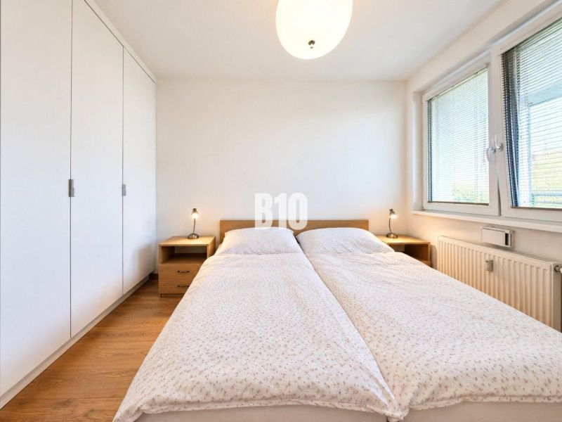 Helles Schlafzimmer mit großem Bett, Kleiderschrank und Boden mit Holzdekor in einer Zweizimmerwohnung.