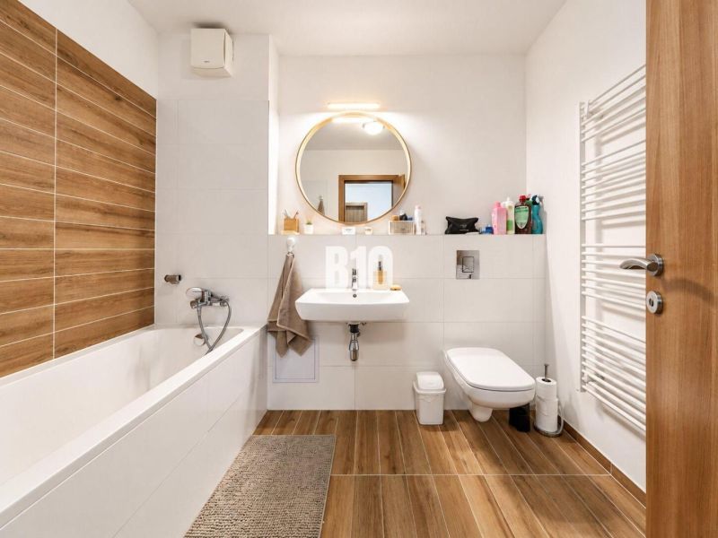 Badezimmer in einer 2-Zimmer-Wohnung mit Badewanne, Waschbecken und Boden mit Holzdekor.