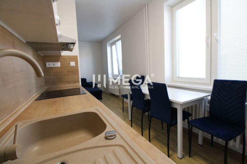 Küche in einer 2-Zimmer-Wohnung mit weißen Möbeln, blauen Stühlen und einem Boden in Holzoptik.